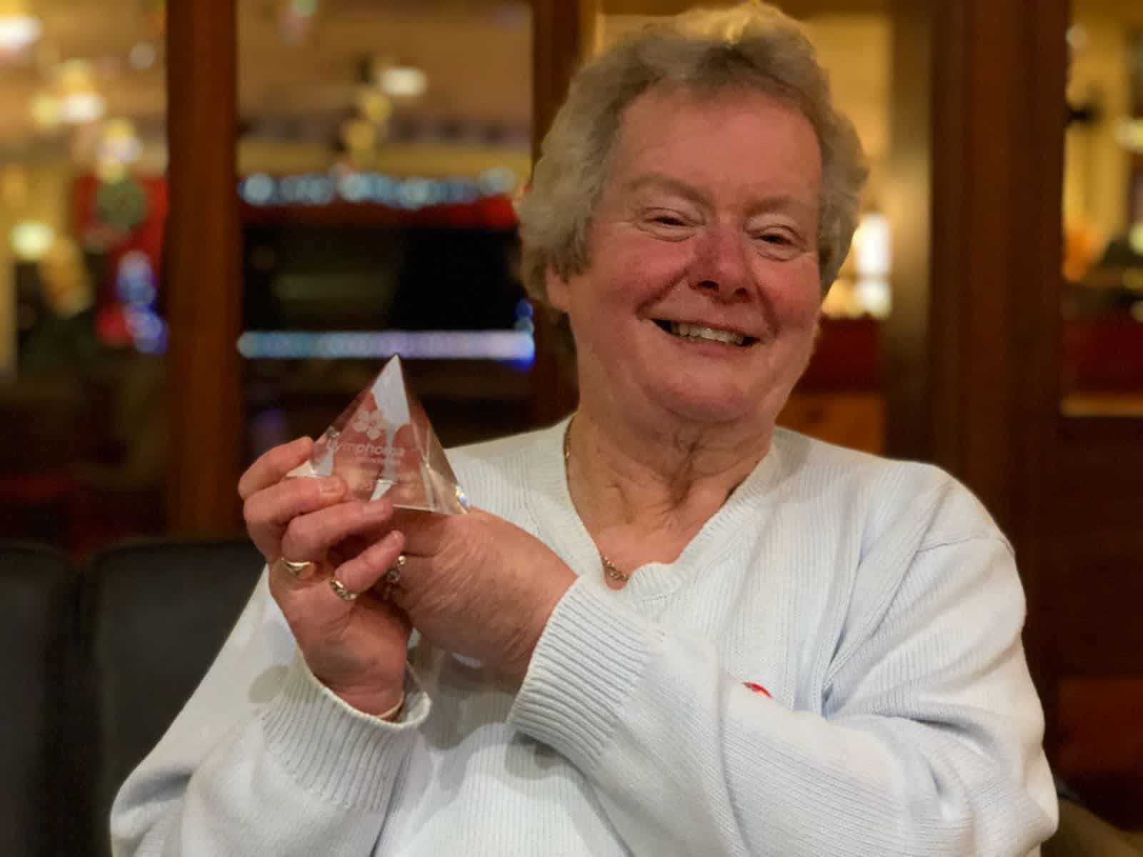 Carol Miller, founder of York Haematology Support group and Acute Myeloid Leukaemia survivor smiling and holding an award from the Lymphoma Association.