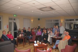 A photo of York Haematology Support Group, taken at one of their meetings. There are around 25 attendees and Carol Miller, founder, sits at the centre of the group, at the back.